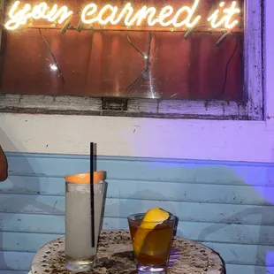 a table with a drink and a neon sign