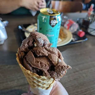 a hand holding a cone of chocolate ice cream