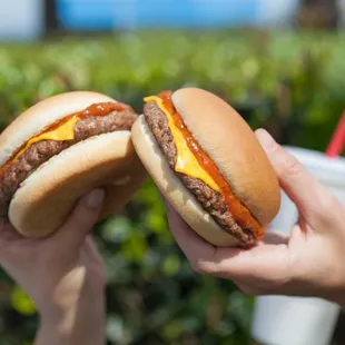two hands holding two hamburgers