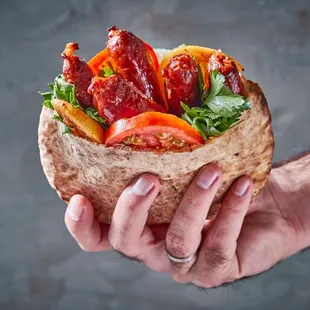 a hand holding a sandwich with bacon, lettuce, tomato, and lettuce