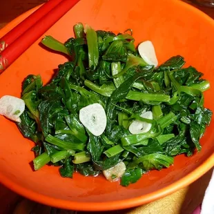 a bowl of greens with chopsticks