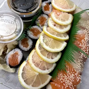 a tray of sushi with salmon and lemon slices