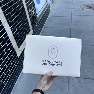 a hand holding a box of doughnuts