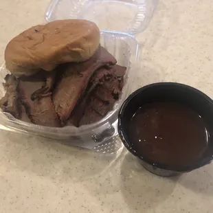 Smoked beef brisket sandwich on bun with a side of tangy BBQ sauce