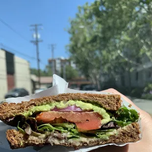 a hand holding a sandwich with lettuce, tomato, and avocado