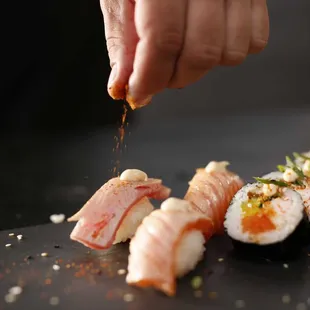 a person sprinkling sauce on sushi