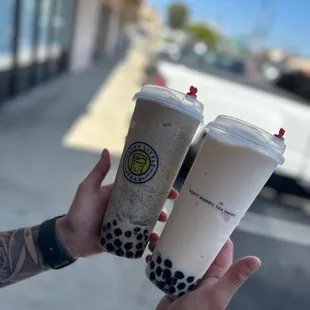 a hand holding two cups of bubble tea