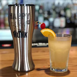 a drink in a glass next to a stainless steel tumbler