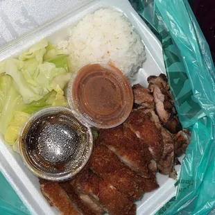 a plastic takeout container filled with meat, rice, lettuce, and sauce