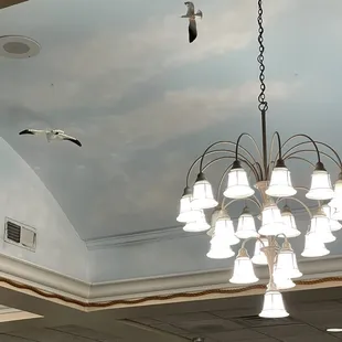 Seagulls suspended from the sky blue ceiling with chandelier lighting.