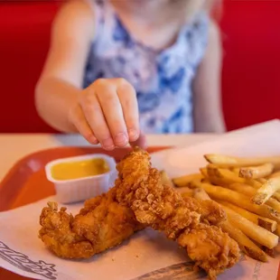 a little girl eating chicken and fries