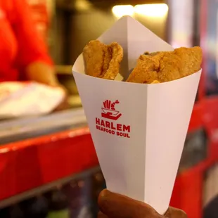 a hand holding a basket of fried food