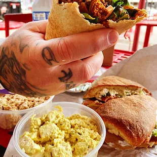 a hand holding a sandwich and a bowl of scrambled eggs