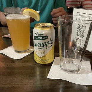a man sitting at a table with a can of pineapple cider and a glass of lemonade