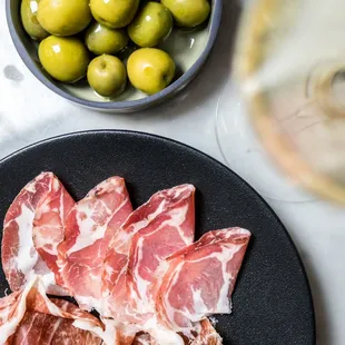 a plate of meat, olives, and a glass of wine