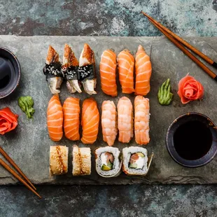 a variety of sushi on a slate board with chopsticks