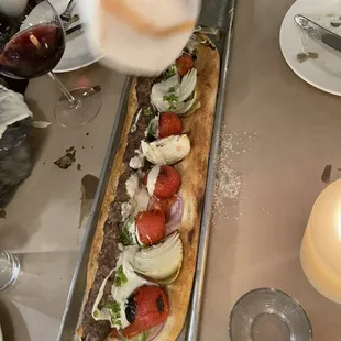 a person putting toppings on a long loaf of bread