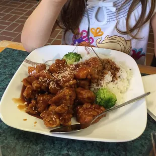 a young girl sitting at a table with a plate of food