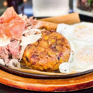 Two eggs over easy with shredded pork and a tamale and plantain with bacon