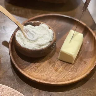 a wooden plate with a bowl of cream and a block of butter
