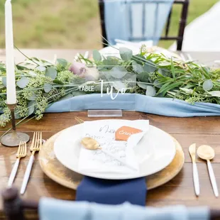 Our dark wood farm table with our Iris charger and Jacqueline flatware and dusty blue chiffon runner.