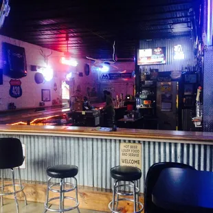 a bar with stools and neon signs
