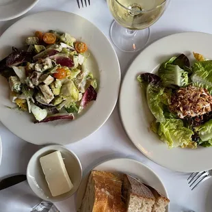 a plate of salad, bread, and a glass of white wine