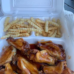 a styrofoam container with chicken wings and french fries