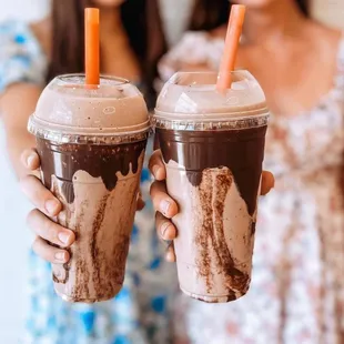 two women holding two cups of iced coffee