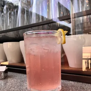 a pink drink in a tall glass with a lemon garnish