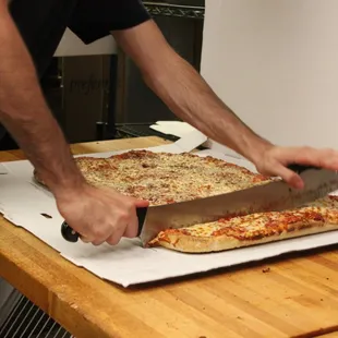 a man cutting a pizza on a cutting board