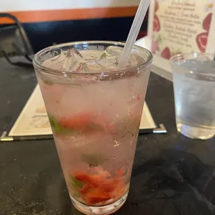 a glass of water with a straw and strawberries in it