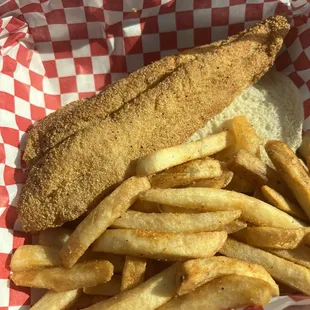 Fried Catfish on a brioche bun, seasoned fries, and pickles that are hidden by the fries.