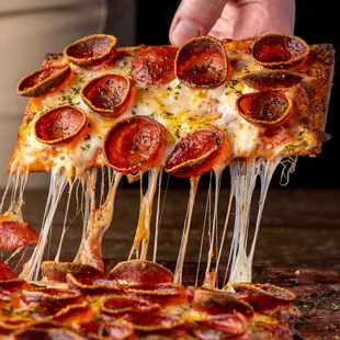 a slice of pepperoni pizza being lifted by a hand