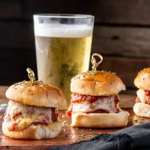 three sliders on a cutting board with a glass of beer in the background