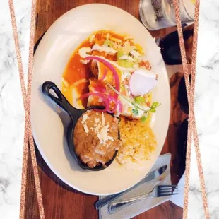 Chicken enchiladas with red sauce, rice, and beans .
