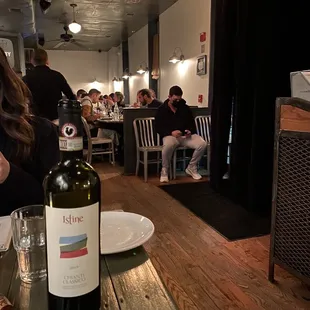 a woman sitting at a table with a bottle of wine