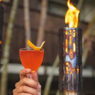 a person holding a cocktail in front of a fire