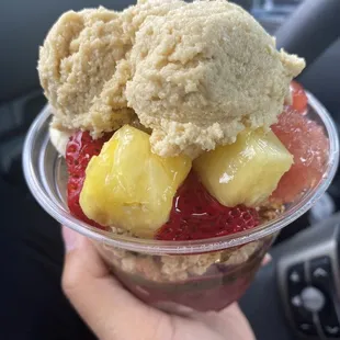 a hand holding a cup of fruit and ice cream