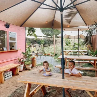 two children sitting at a picnic table under an umbrella