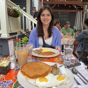 a woman sitting at a table with pancakes and eggs