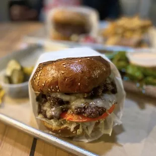 Double Cheeseburger ($9.95), Shishito Peppers ($4.75), Double Burger ($8.95 + $1.50 avocado), Fries ($2.95). Two tables outside.