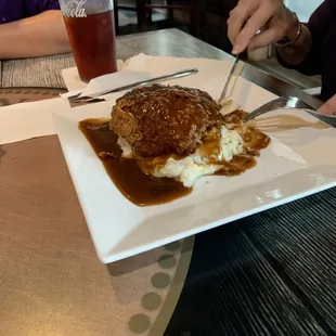 Fried chicken breast and gravy over mashed potatoes.
