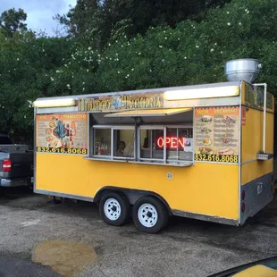 Cute yellow taco truck. With delicious foods being made inside.