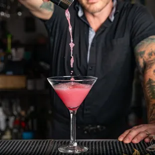 a bartender pouring a pink cocktail