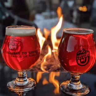 two glasses of beer in front of a fire