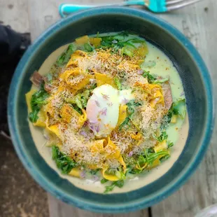 House-made tagliatelle, asparagus, garlic cream, poached egg, prosciutto, chives, breadcrumbs garnished with tiny flowers.