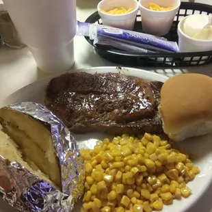 Steak dinner with baked potatoes, corn and a roll