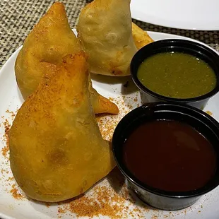 a plate of empanadas with dipping sauces