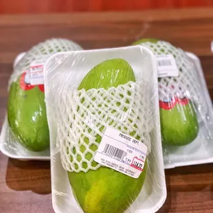 three green mangoes wrapped in plastic